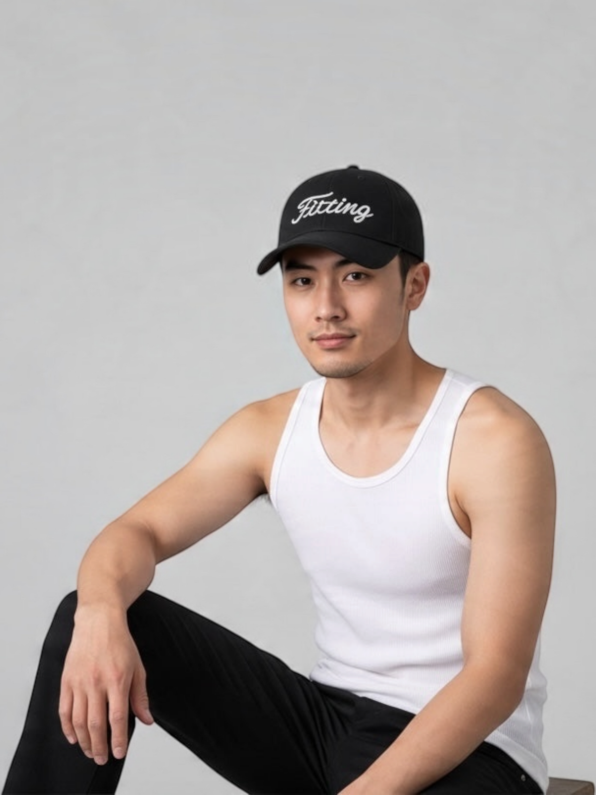A man wearing a FITTING black baseball cap with a white embroidered logo, paired with a white tank top.