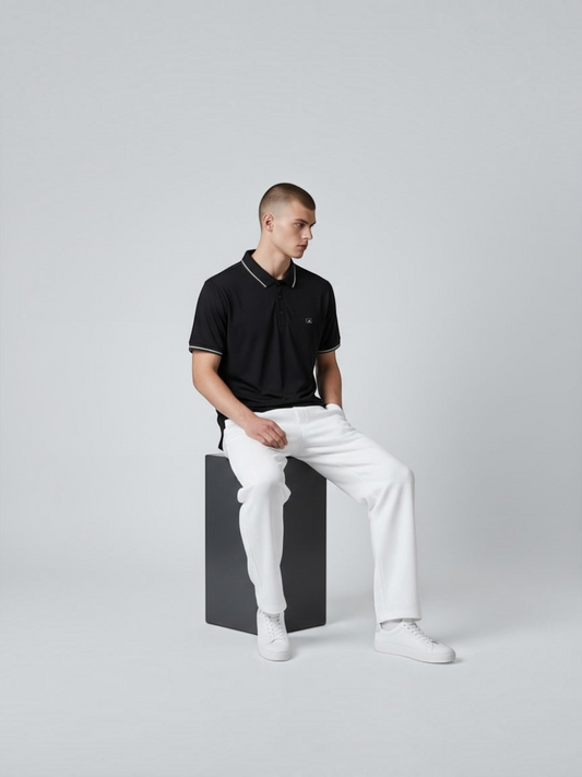 A man wearing a FITTING black performance polo shirt with white contrast tipping, paired with white trousers.