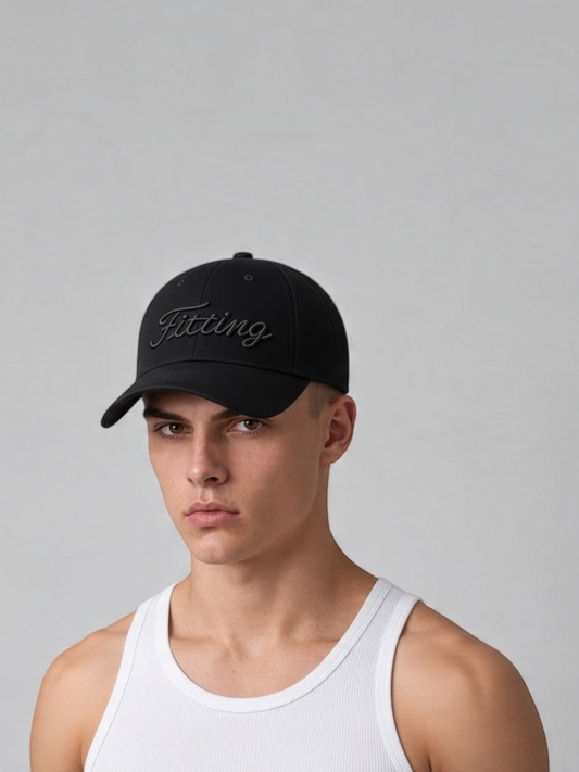 A man wearing a FITTING black baseball cap with tonal embroidered script, featuring a minimalist six-panel design.