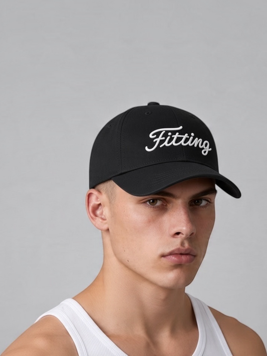 A man wearing a black FITTING baseball cap with a white embroidered logo on the front against a grey background.