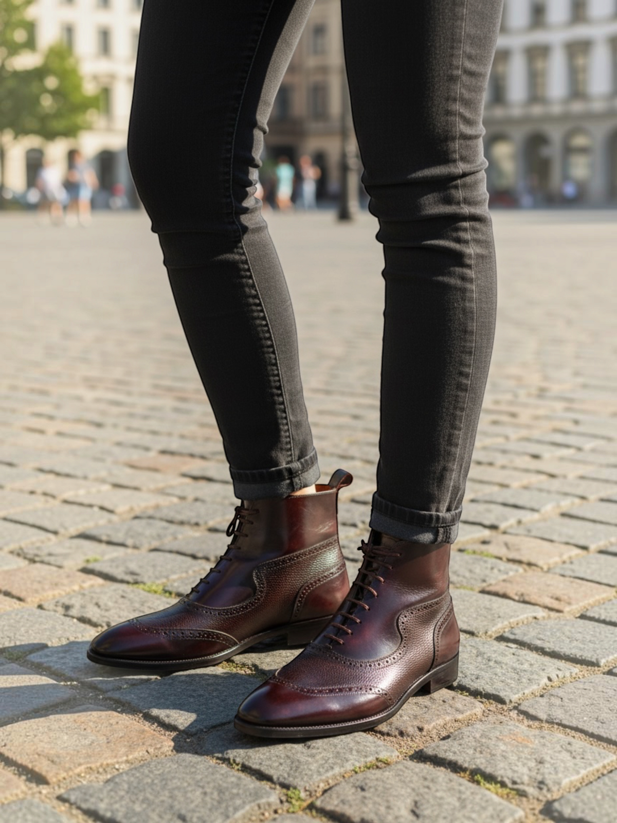 FITTING men's burgundy leather brogue ankle boots with lace-up closure worn with dark grey jeans on a cobblestone street